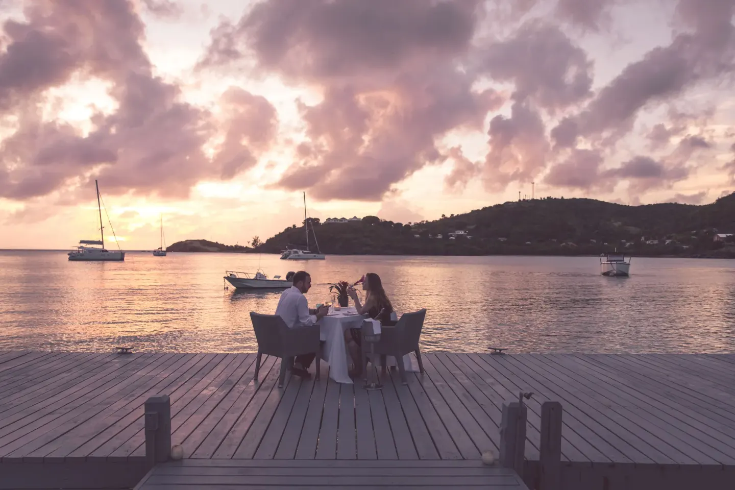 Couple dining on a wooden jetty at sunset over the bay at Carlisle Bay.