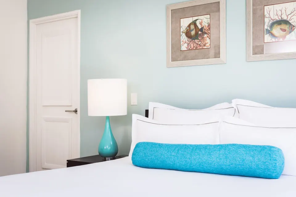 King bed in a beach balcony suite bedroom at Carlisle Bay with fish artwork and turquoise accents.