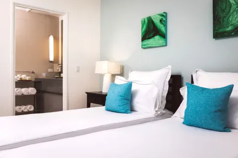 Twin beds in a beach balcony suite at Carlisle Bay with the bathroom doorway visible beyond.
