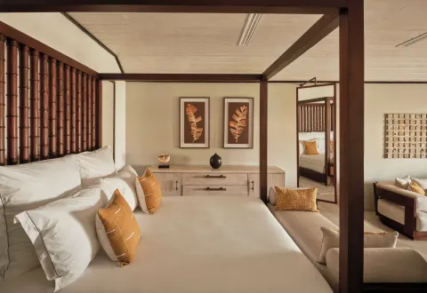 Garden Suite bedroom with four-poster bed, pillows and sitting area at Carlisle Bay.