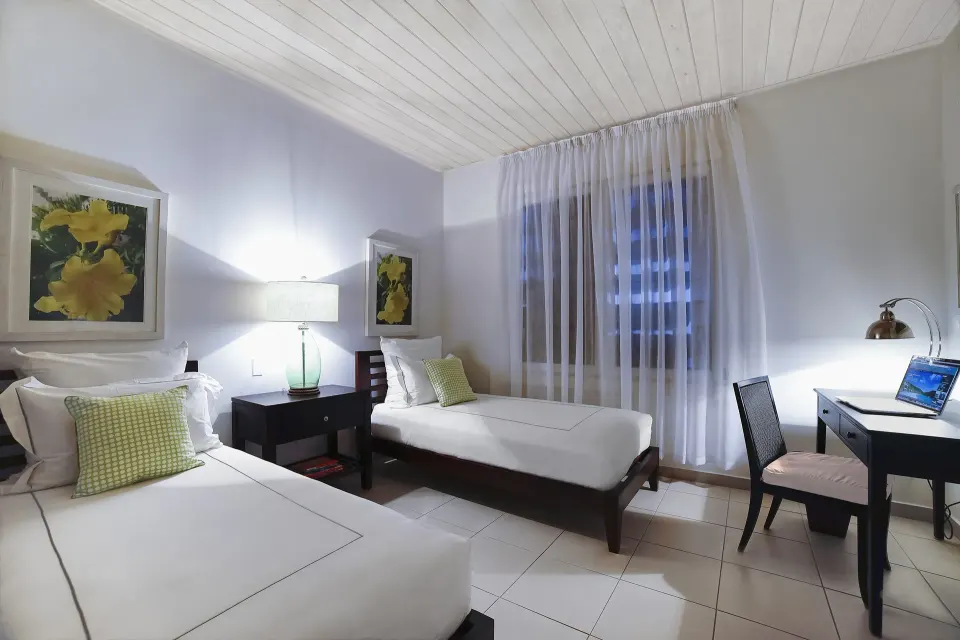 Twin beds and a writing desk in a Terrace beach suite bedroom at Carlisle Bay.