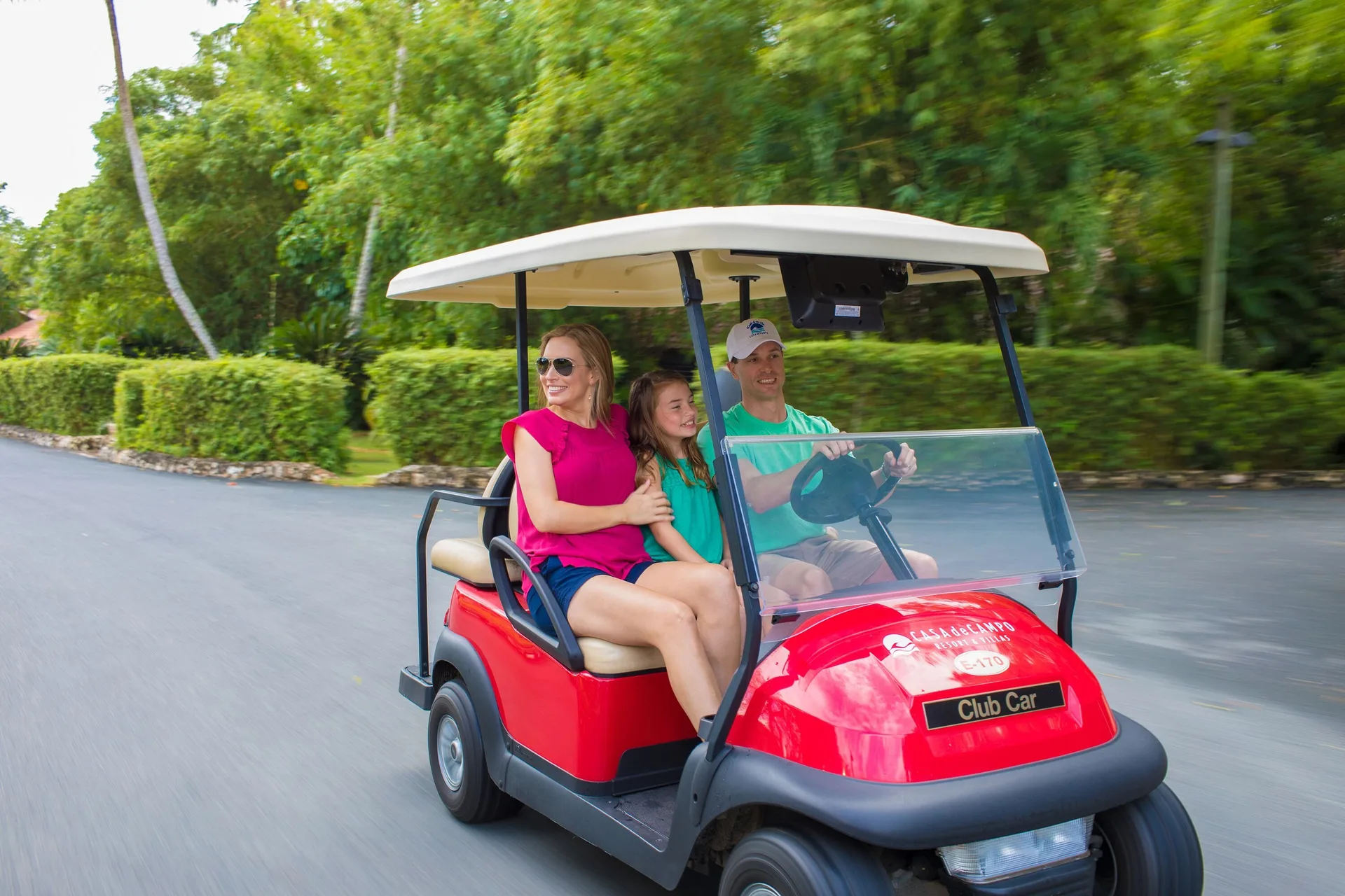 Guests ride a red golf cart along a road at Casa de Campo Resort and Villas.
