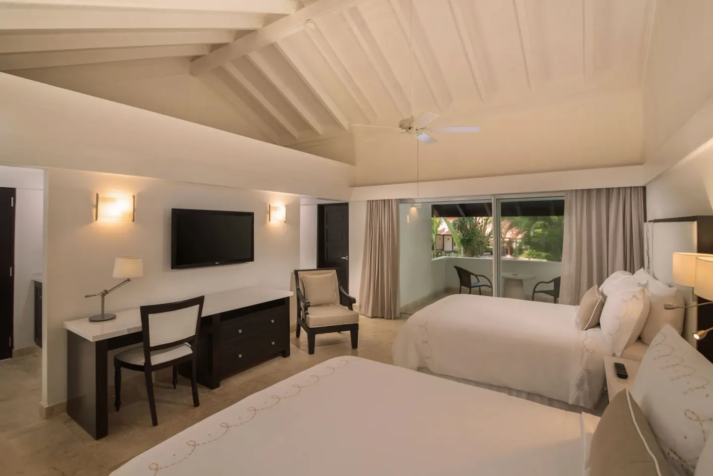 Guest room with two beds, desk, TV, and balcony at Casa de Campo Resort and Villas.
