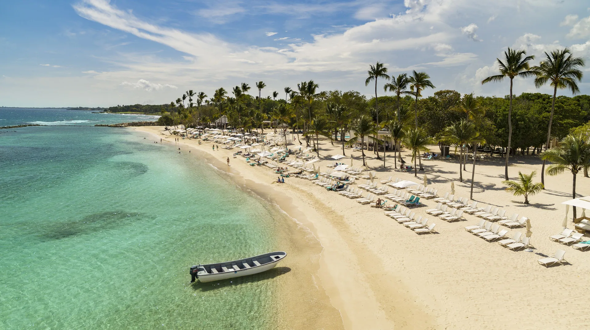 Palm-lined beach with loungers and a small boat at Casa de Campo Resort and Villas.