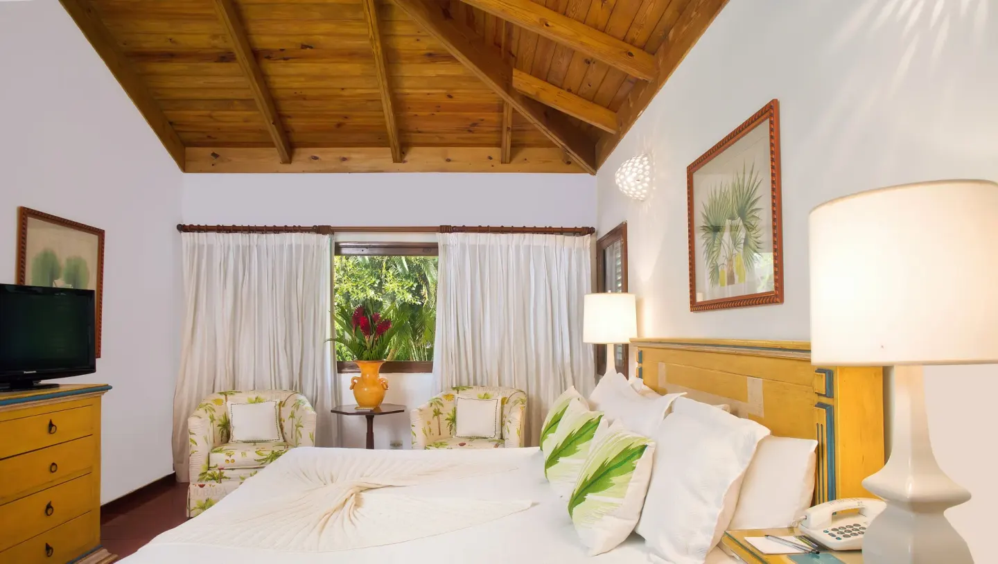 Bedroom with white bed, green accents, and wood ceiling at Casa de Campo Resort and Villas and Villas and Villas.