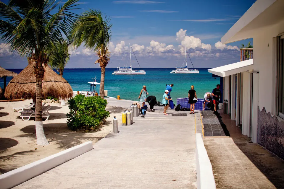 Resort beachfront walkway with palms, guests and boats at Casa del Mar Cozumel Hotel & Dive Resort