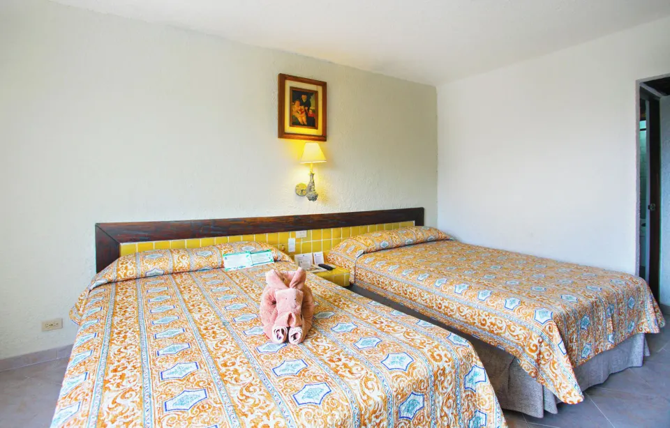 Two patterned-bedspread beds with towel animal on one bed in a guest room at Casa del Mar Cozumel Hotel & Dive Resort