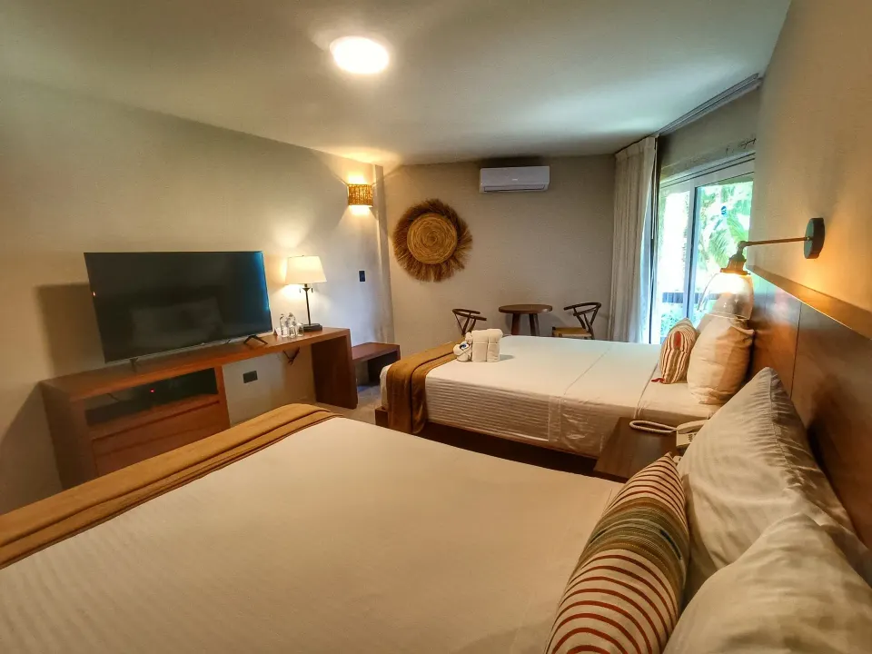 Two beds facing a TV and sliding glass door in a guest room at Casa del Mar Cozumel Hotel & Dive Resort