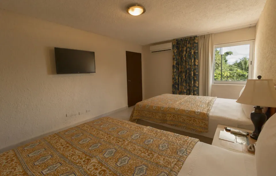 Two double beds, wall TV and window in a guest room at Casa del Mar Cozumel Hotel & Dive Resort