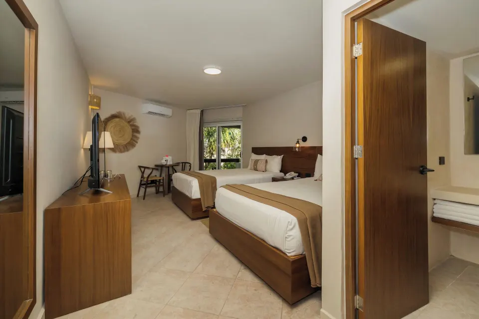 View from doorway into a twin-bedded guest room with TV and bathroom entry at Casa del Mar Cozumel Hotel & Dive Resort