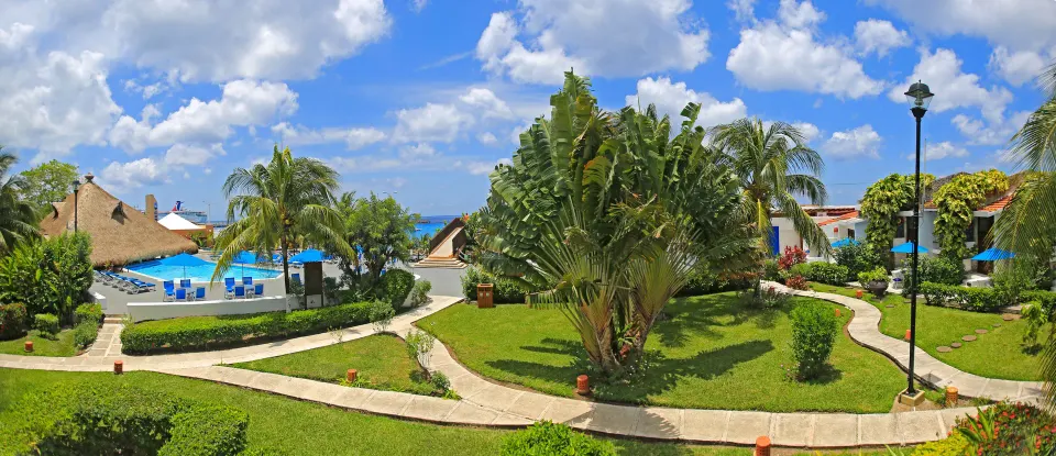 Landscaped gardens with pathways and a pool area at Casa del Mar Cozumel Hotel & Dive Resort
