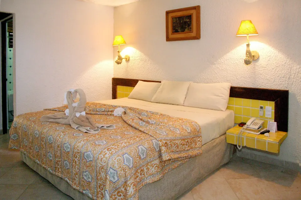 Guest room with king bed, bedside lamps and decorated towel at Casa del Mar Cozumel Hotel & Dive Resort.