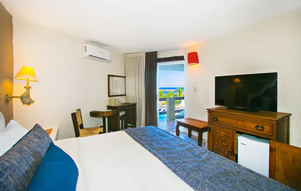 Guest room with balcony view of pool and ocean and wooden TV cabinet at Casa del Mar Cozumel Hotel & Dive Resort