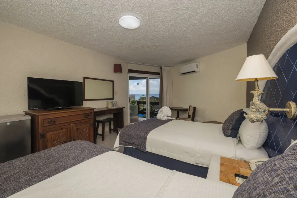 Twin beds in a guest room with balcony view of the water at Casa del Mar Cozumel Hotel & Dive Resort