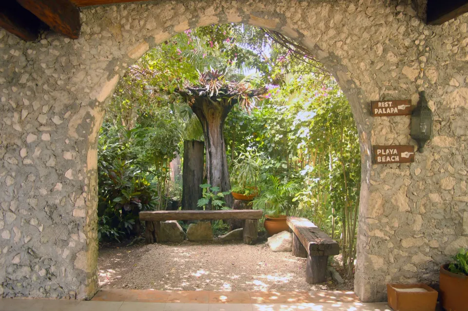 Stone archway framing a shaded garden seating area at Casa del Mar Cozumel Hotel & Dive Resort