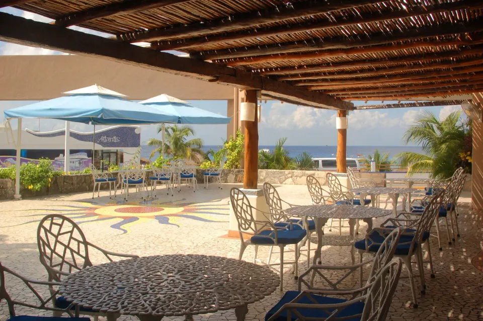 Shaded terrace dining area with wrought-iron tables overlooking the ocean at Casa del Mar Cozumel Hotel & Dive Resort