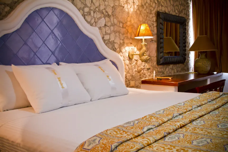Close-up of a made bed with patterned cover and textured stone wall at Casa del Mar Cozumel Hotel & Dive Resort