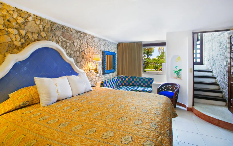 Guest room with king bed, patterned bedspread and seating area at Casa del Mar Cozumel Hotel & Dive Resort
