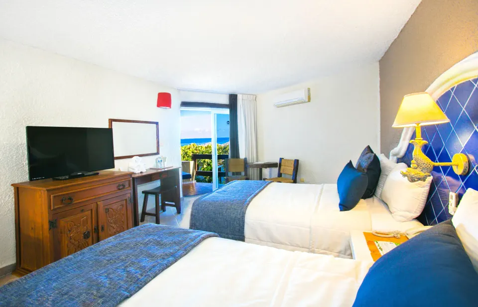 Twin beds and sliding door with a partial ocean view in a guest room at Casa del Mar Cozumel Hotel & Dive Resort