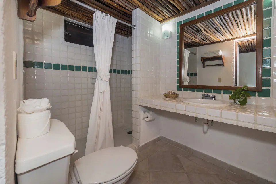 Bathroom with tiled countertop, shower with curtain and wooden ceiling at Casa del Mar Cozumel Hotel & Dive Resort
