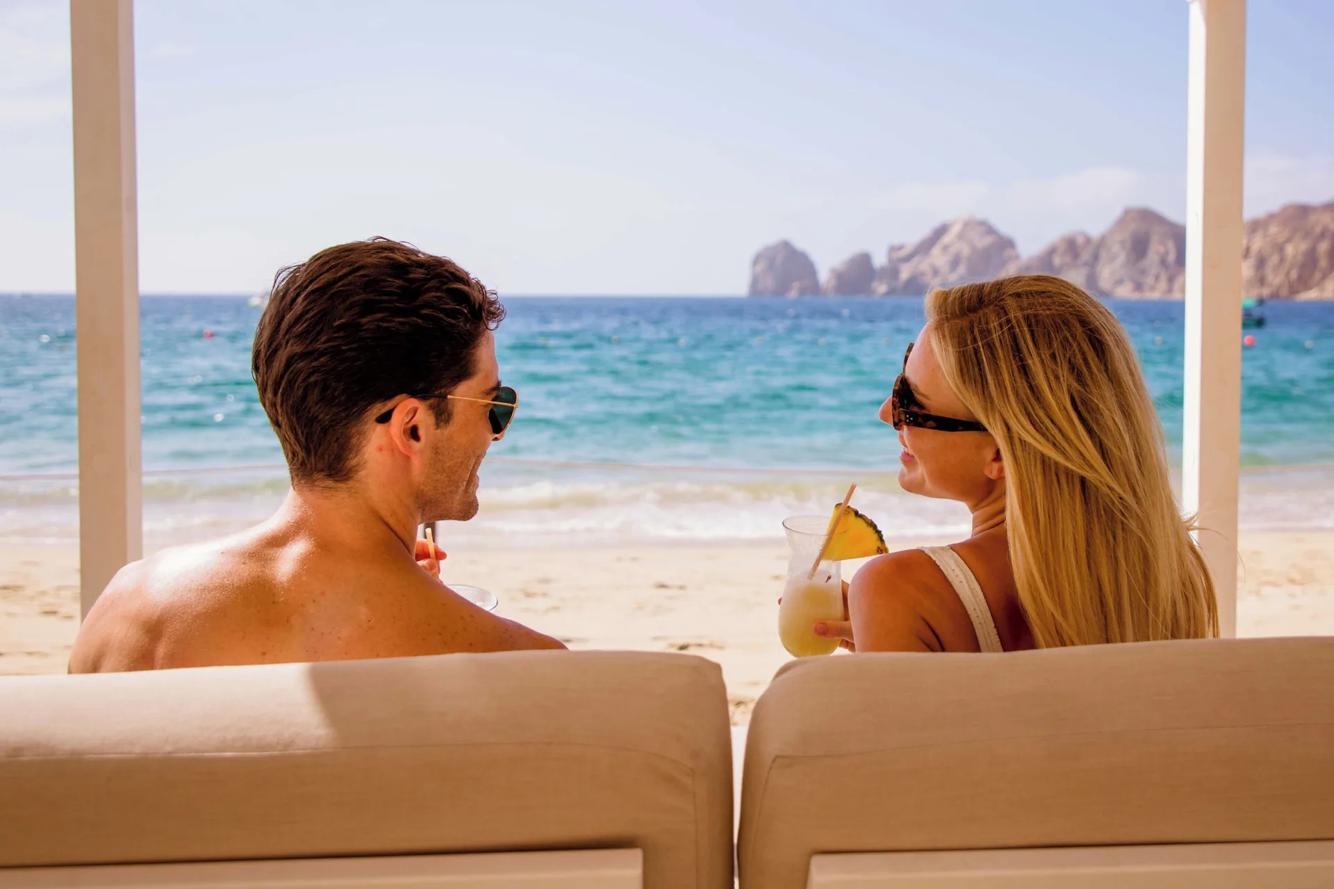 Couple seated by the beach with drinks at Casa Dorada Los Cabos Resort & Spa.