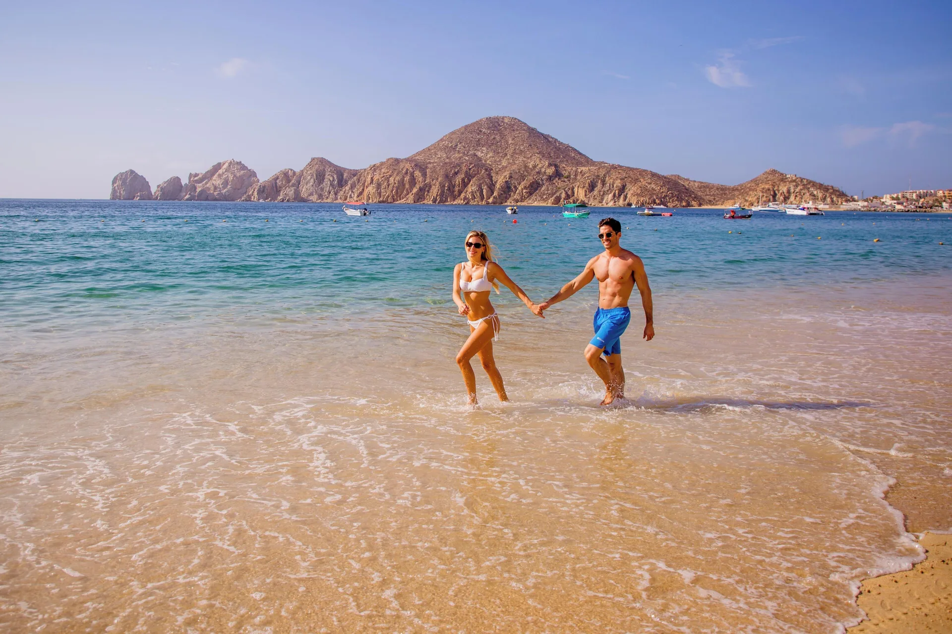 Couple walking in the surf near Casa Dorada Los Cabos Resort & Spa with rocky headland beyond.
