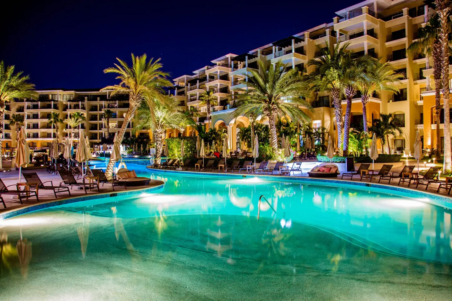 Nighttime pool with palm trees and illuminated buildings at Casa Dorada Los Cabos Resort & Spa.