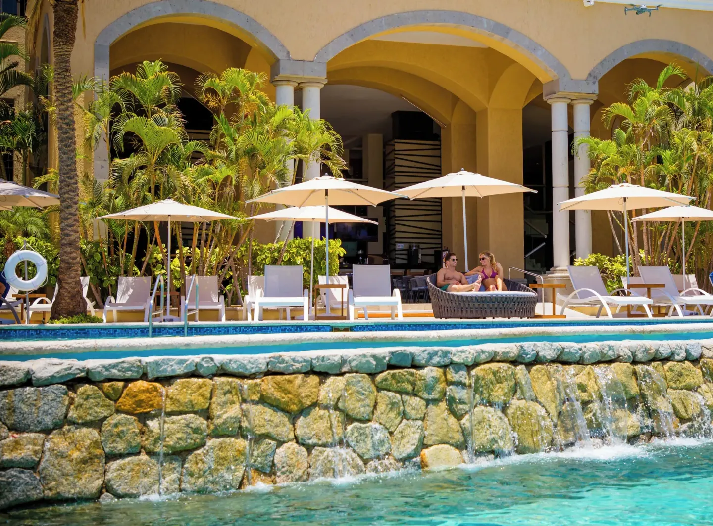 Poolside terrace with umbrellas and stone waterfall at Casa Dorada Los Cabos Resort & Spa.