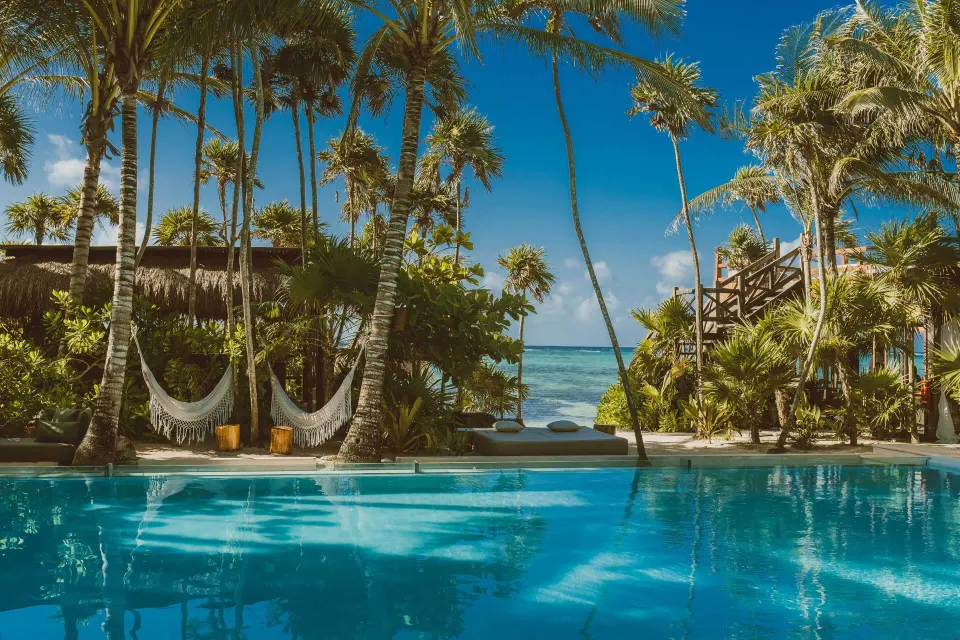 Jashita Hotel upscale boutique beachfront hotel with calm bay water, white sand, and palapa loungers on Soliman Bay, Mexico.