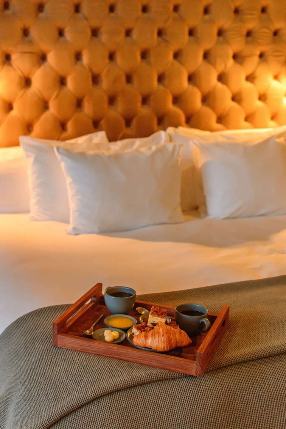 Tray with croissant and coffee on a bed with tufted headboard at Casa Malca