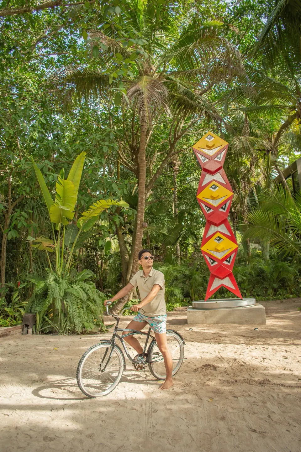 Guest on a bicycle paused beside a colorful totem sculpture in the gardens at Casa Malca.