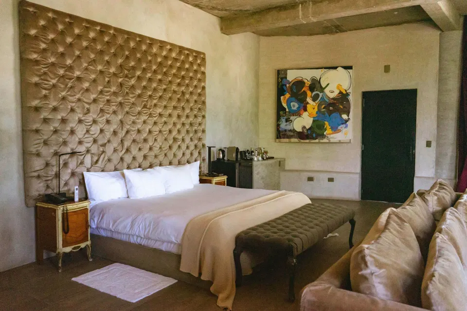 King bed with oversized tufted headboard and abstract painting in a guest room at Casa Malca