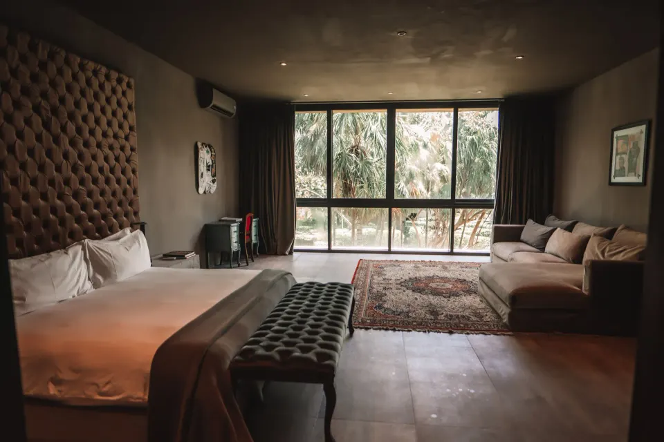 Dimly lit suite with king bed, tufted bench and wide window view at Casa Malca