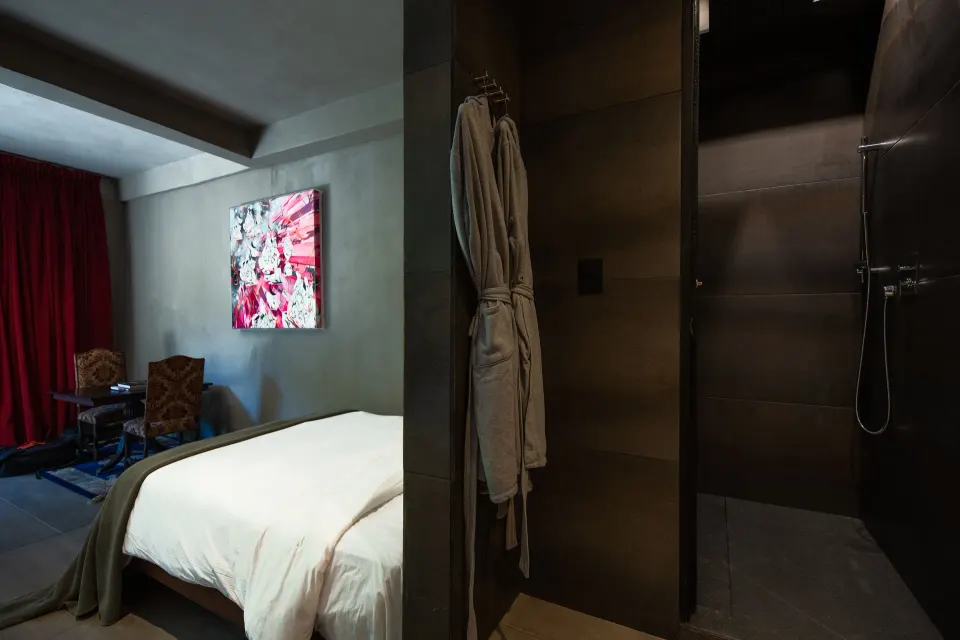 Guest room view showing king bed, wall art and an open dark-tiled shower at Casa Malca