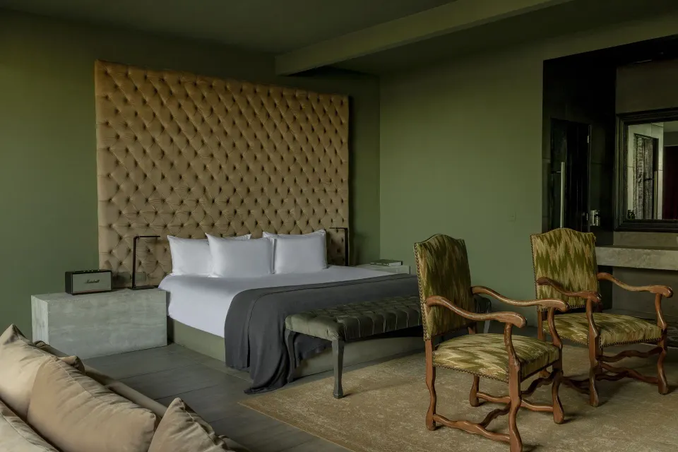 King bed with tall beige tufted headboard and two antique chairs at Casa Malca