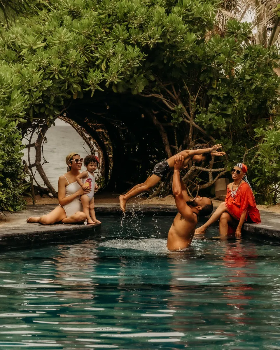 Family playing in a resort pool under a leafy arch at Casa Malca.