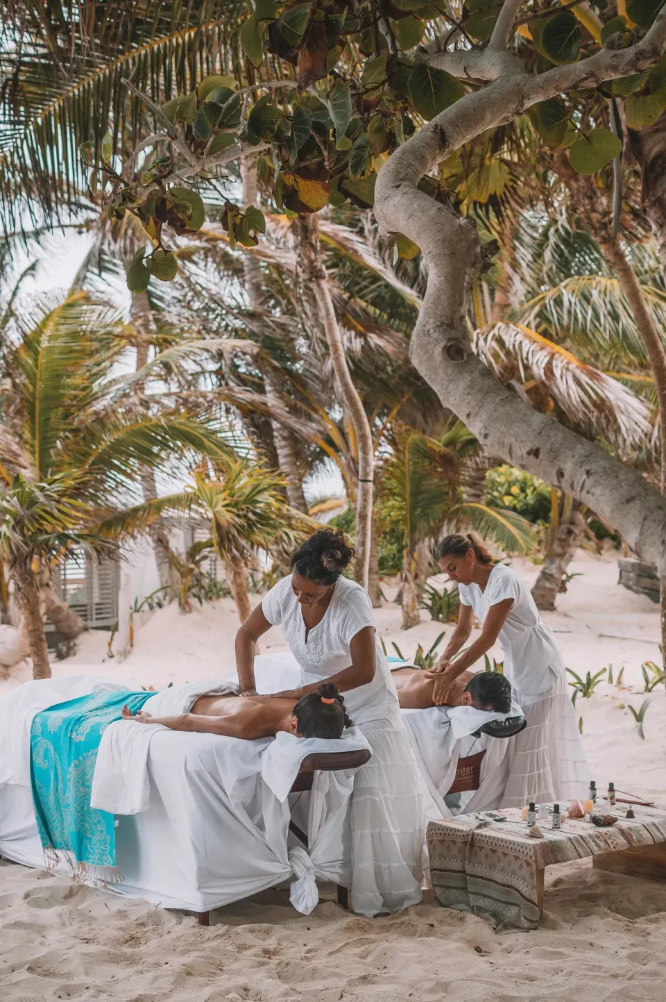 Two therapists giving beachside massages under trees at Casa Malca spa.