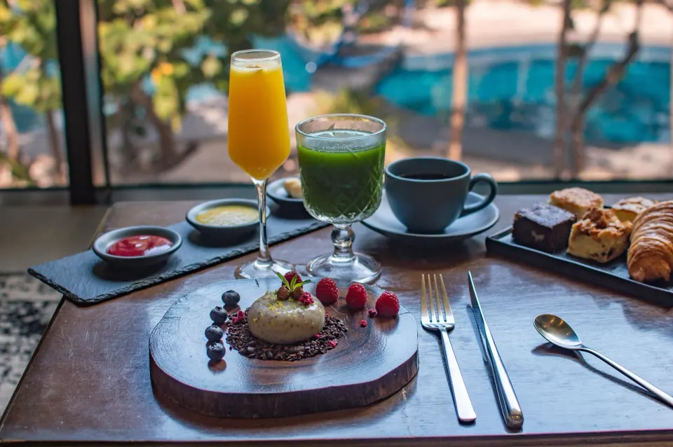 Breakfast tray with juice and pastries by a window overlooking the pool at Casa Malca