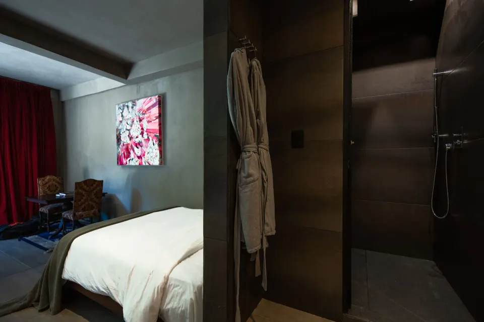 Guest room shower entry with robes hanging near a bed and dark tile at Casa Malca