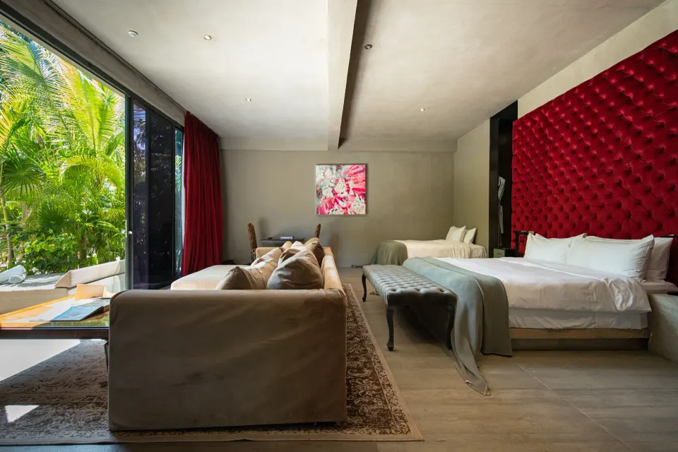 Family Suite interior facing garden with king bed, sofa and red tufted wall at Casa Malca