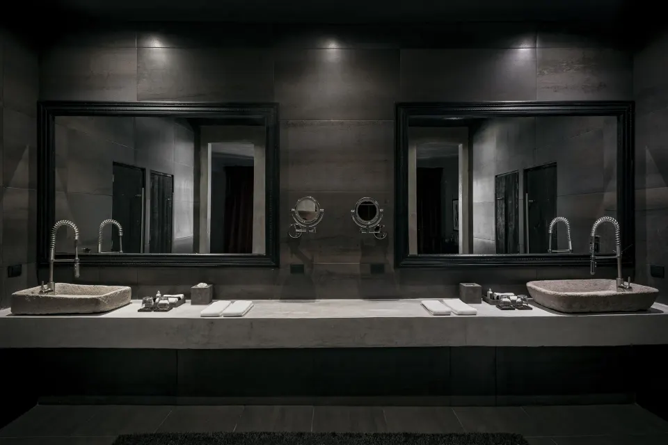Dimly lit bathroom in the Family Suite with twin stone sinks and large black-framed mirrors at Casa Malca