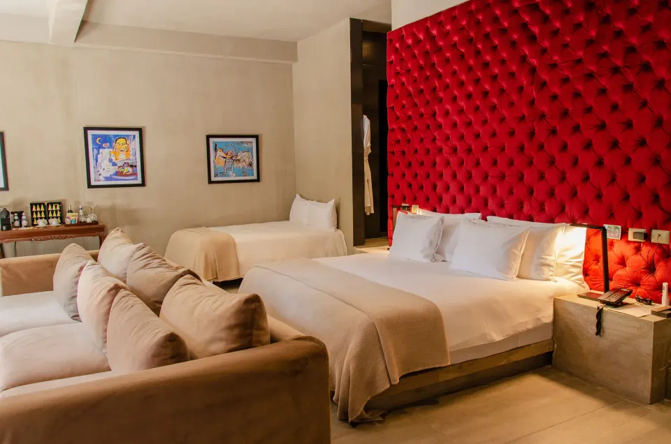 Family Suite with king bed, sofa and artwork beside the red tufted wall at Casa Malca