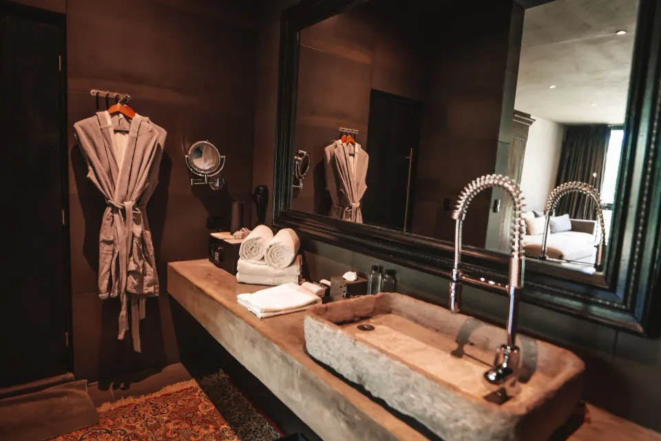 Stone sink and vanity in the Junior Suite Beachfront bathroom at Casa Malca, with robes hung nearby.