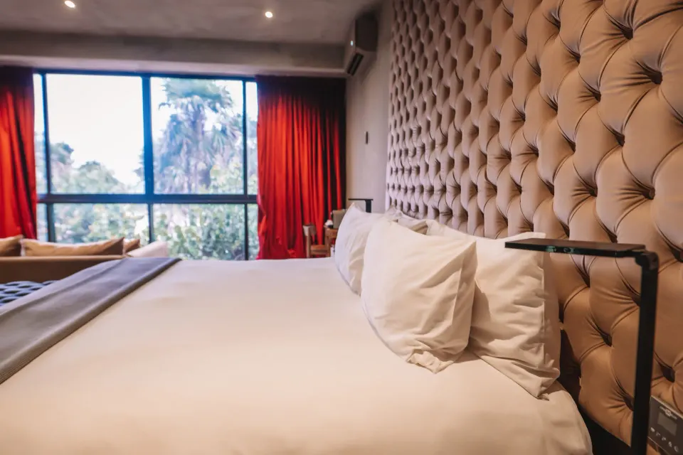 Close-up of king bed with tufted headboard and red curtains framing a view at Casa Malca