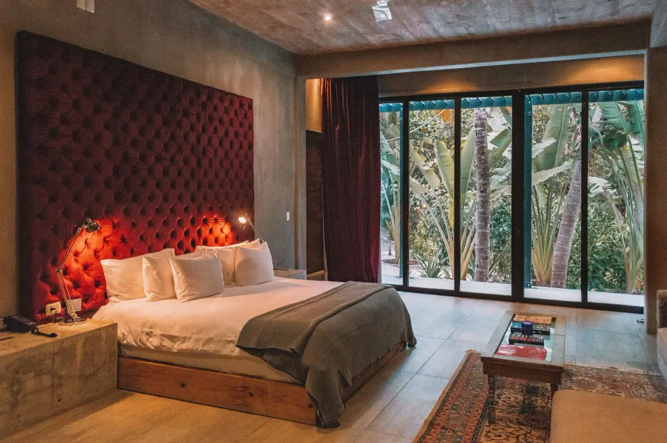 Junior Suite Garden View at Casa Malca showing bed with red tufted headboard and tall glass doors to the garden