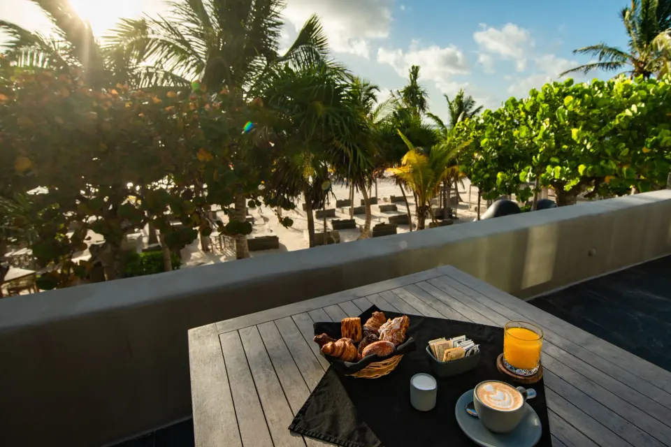Breakfast tray on a terrace overlooking Casa Malca's palm-lined beachfront and lounge chairs.