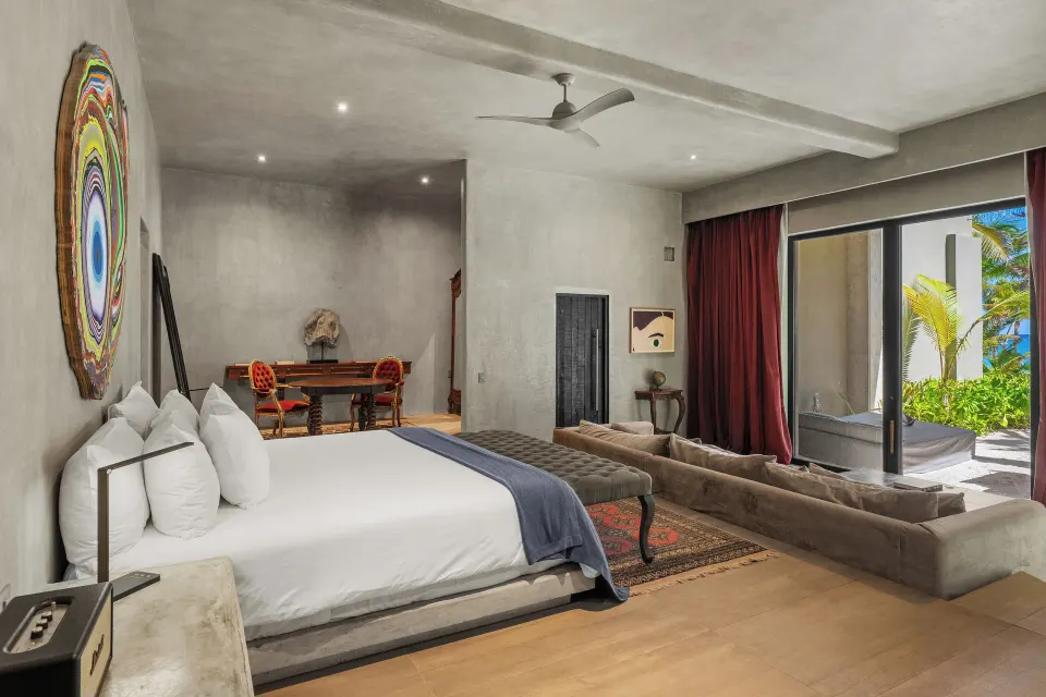 Master suite with king bed, low sofa and sliding doors to a lush garden at Casa Malca