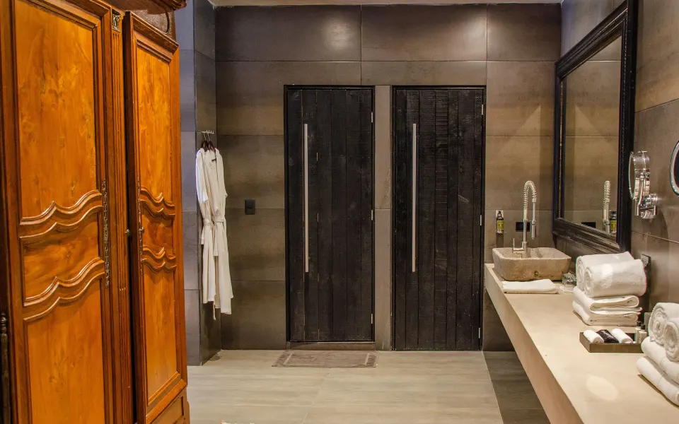 Suite bathroom corridor with dark double doors, wooden armoire and folded towels at Casa Malca.
