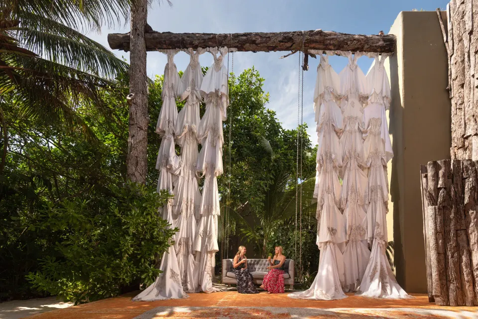 Two women seated beneath a large wooden swing and hanging fabric at Casa Malca.