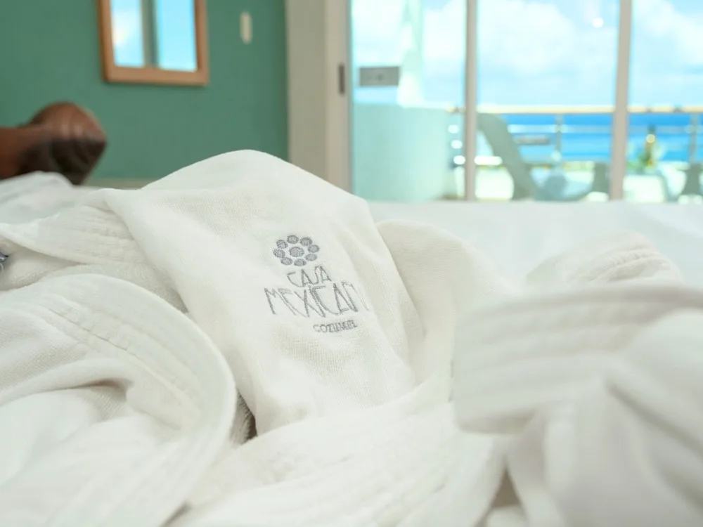 Close-up of a white bathrobe on a bed at Casa Mexicana Cozumel with balcony and ocean beyond